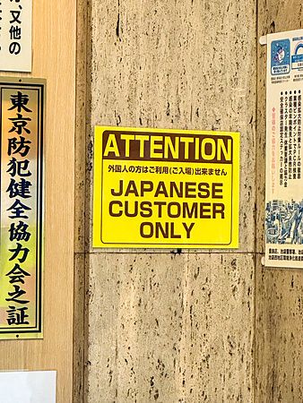 Cartello giallo con scritta "Japanese customer only" su un muro in Giappone.