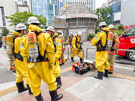 Pompieri in tute gialle a Shinjuku, Giappone, riuniti davanti a un edificio.