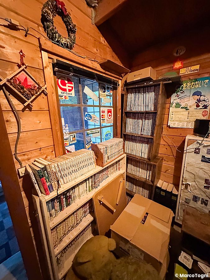 Interno di biblioteca in legno con scaffali pieni di manga in un campeggio giapponese.