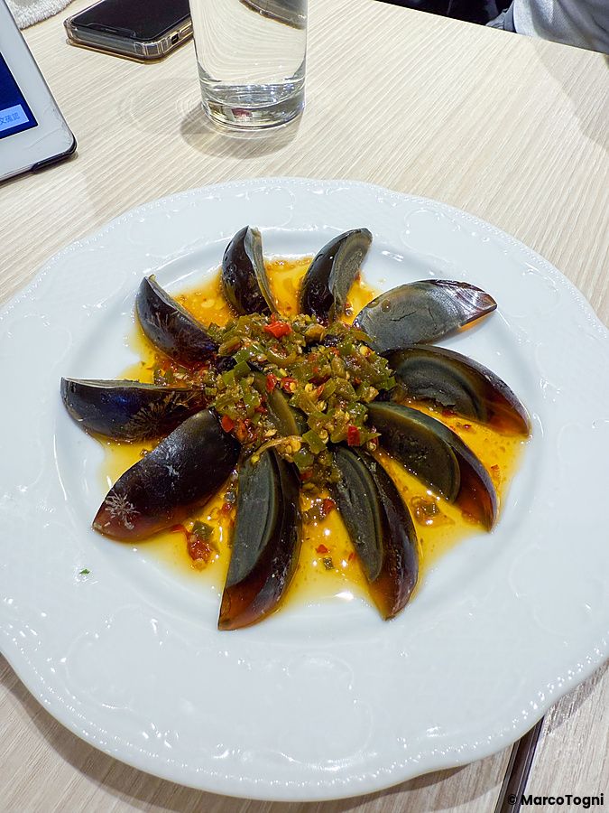 Spicchi di uovo nero cinese conditi con peperoncini al centro di un piatto bianco presso il ristorante Mara Daigaku.