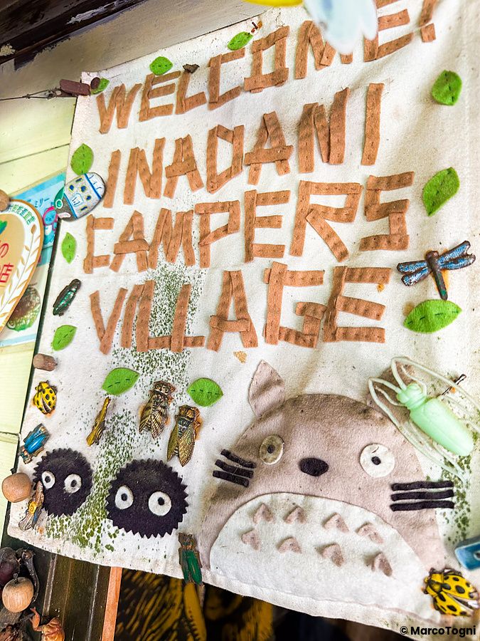 Cartello artigianale con scritta "benvenuto a Inadani Campers Village" e disegni.
