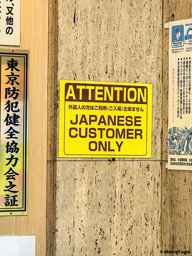 Cartello giallo con scritta "Japanese customer only" su un muro in Giappone.