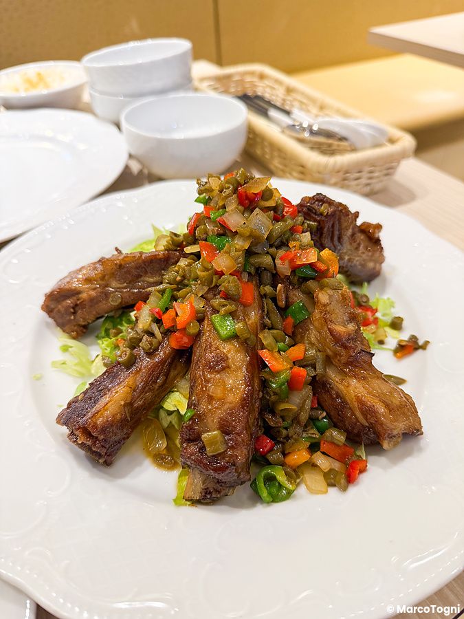 Costine di maiale in stile cinese con verdure tritate in un piatto bianco presso il ristorante Mara Daigaku.
