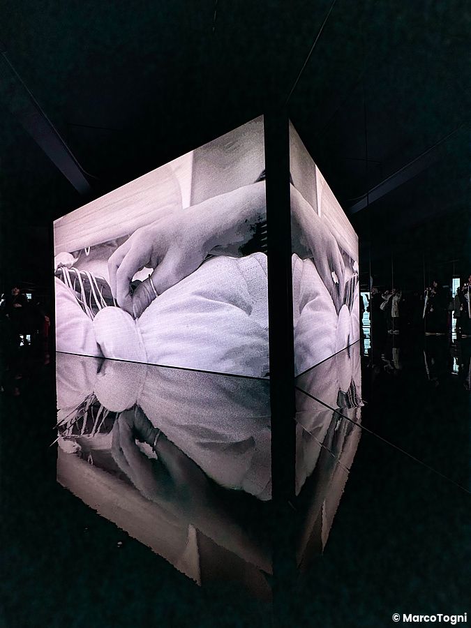 Installazione video angolare alla Mostra di Maison Margiela a Tokyo che proietta immagini di mani e tessuti.