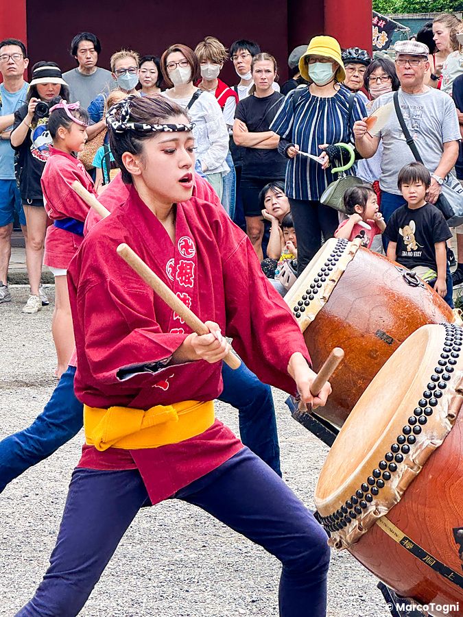 Una donna in costume tradizionale suona un tamburo taiko al santuario Nezu a Tokyo, in Giappone, circondata da spettatori.