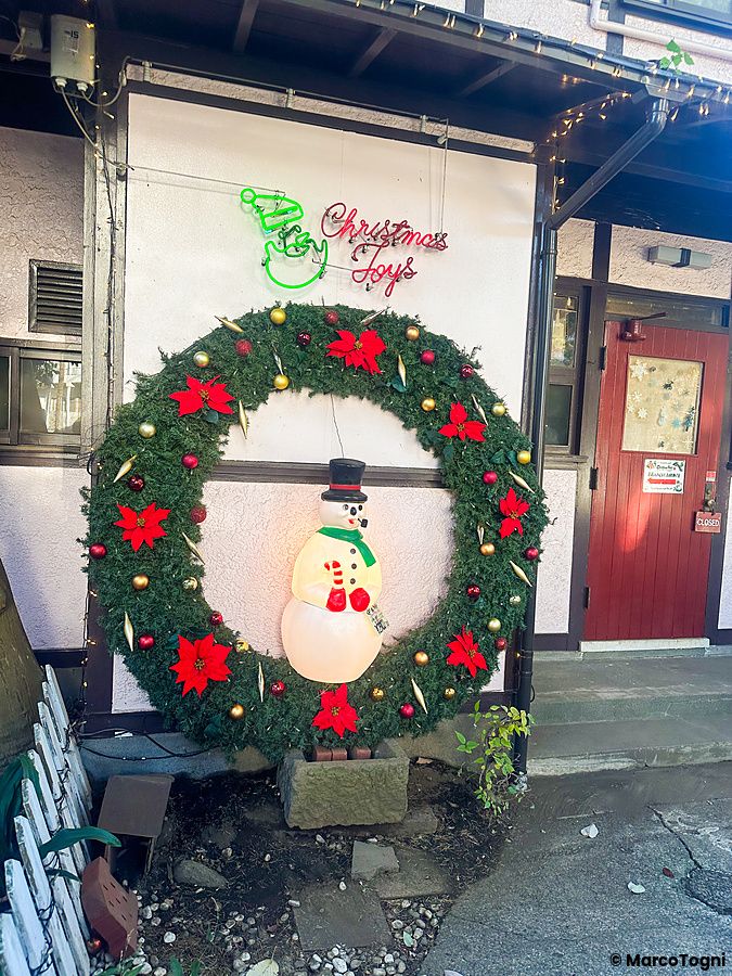 Esterno del negozio Christmas Toys a Yokohama con una grande ghirlanda natalizia e un pupazzo di neve illuminato.