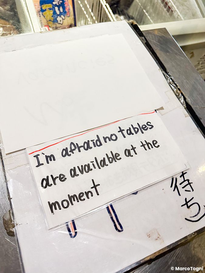 Cartello scritto a mano in un locale giapponese indicando l'assenza di tavoli disponibili.
