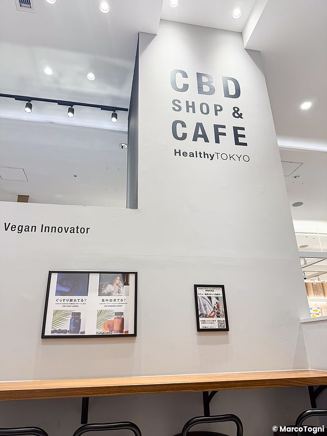 Interno del negozio e caffè HealthyTokyo a Tokyo, con insegna a parete che indica CBD Shop & Cafe e stile minimalista.