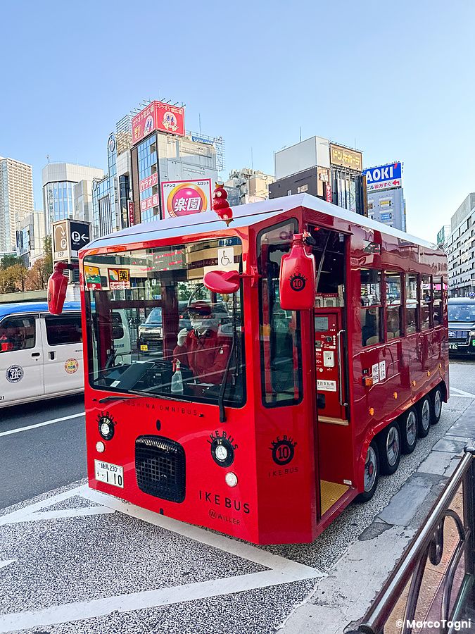 Un piccolo autobus rosso IKEBUS fermo in una strada di Ikebukuro con una persona alla guida.