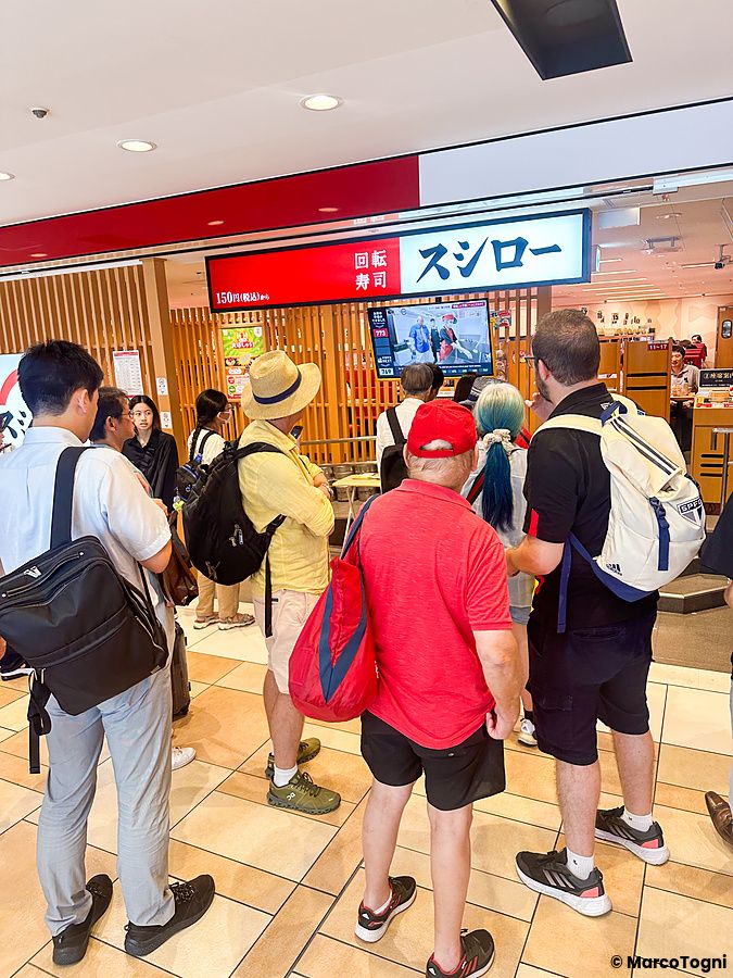 Persone in fila davanti all'ingresso di Sushiro nella stazione di Tokyo (uscita Yaesu).