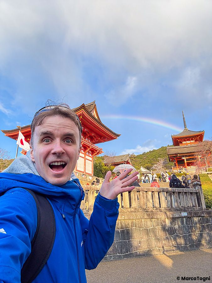 Marco Togni con giacca blu scatta un selfie davanti a Kiyomizudera con arcobaleno.
