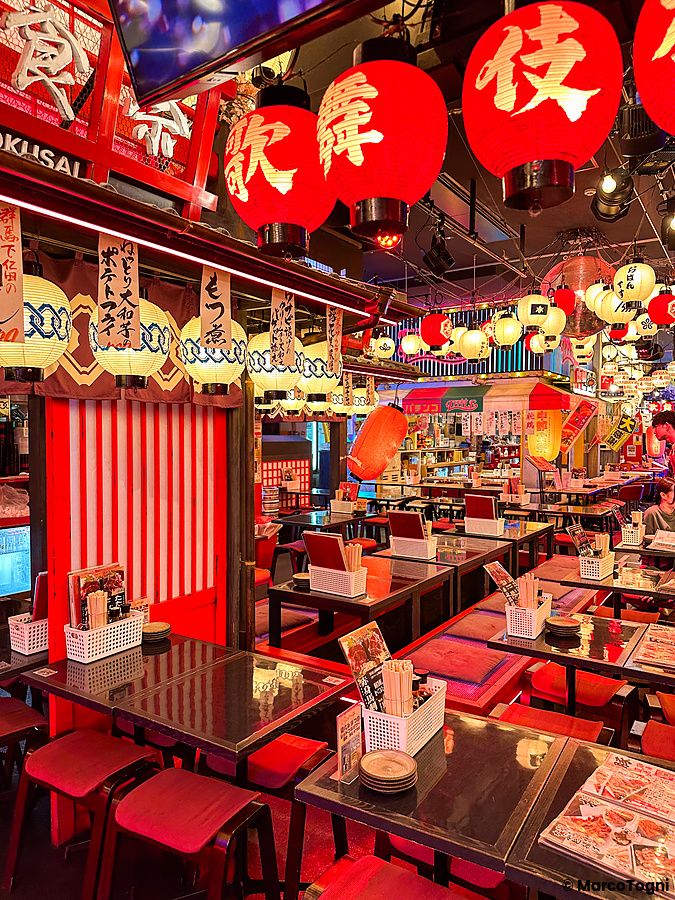 Interno di un ristorante nella Kabukicho Tower a Shinjuku con tavoli, sedie rosse e numerosi lampioncini appesi al soffitto.