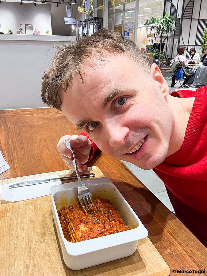Marco Togni sorride davanti a una porzione di lasagna vegana servita in una pirofila bianca presso HealthyTokyo.