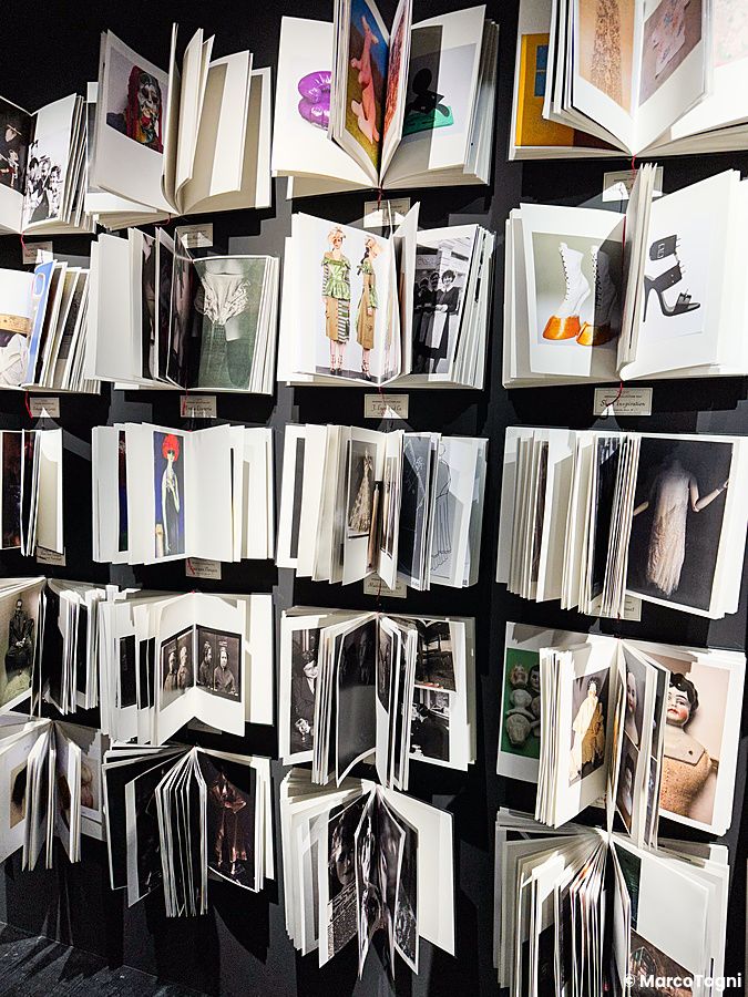 Libri aperti con immagini di moda appesi a una parete nera durante la mostra di Maison Margiela a Tokyo.