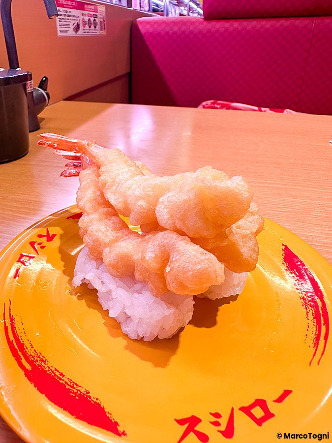 Un nigiri con gambero fritto servito su un piatto giallo con il logo di Sushiro in un ristorante.