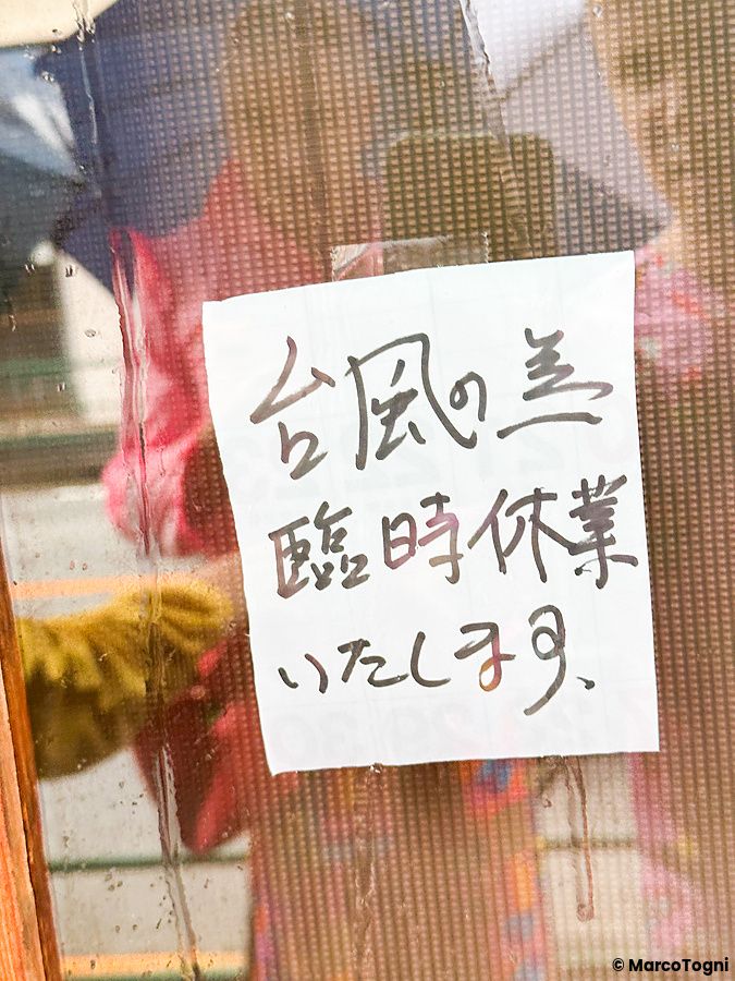 nota scritta in giapponese su finestra bagnata, con persona e ombrello dietro.