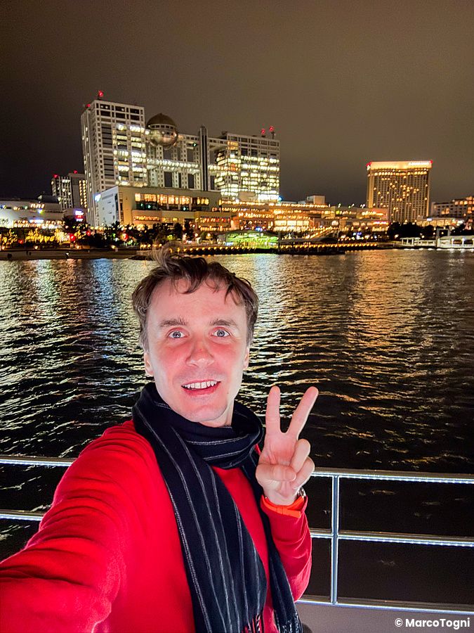 Marco Togni fa il segno di vittoria a bordo di una Yakatabune con vista dalla barca vicino ad Odaiba, Tokyo, di notte.