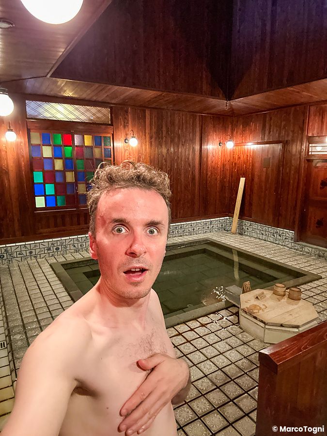 Marco Togni in un onsen interno a Yamashiro Onsen, con pareti di legno e piastrelle.