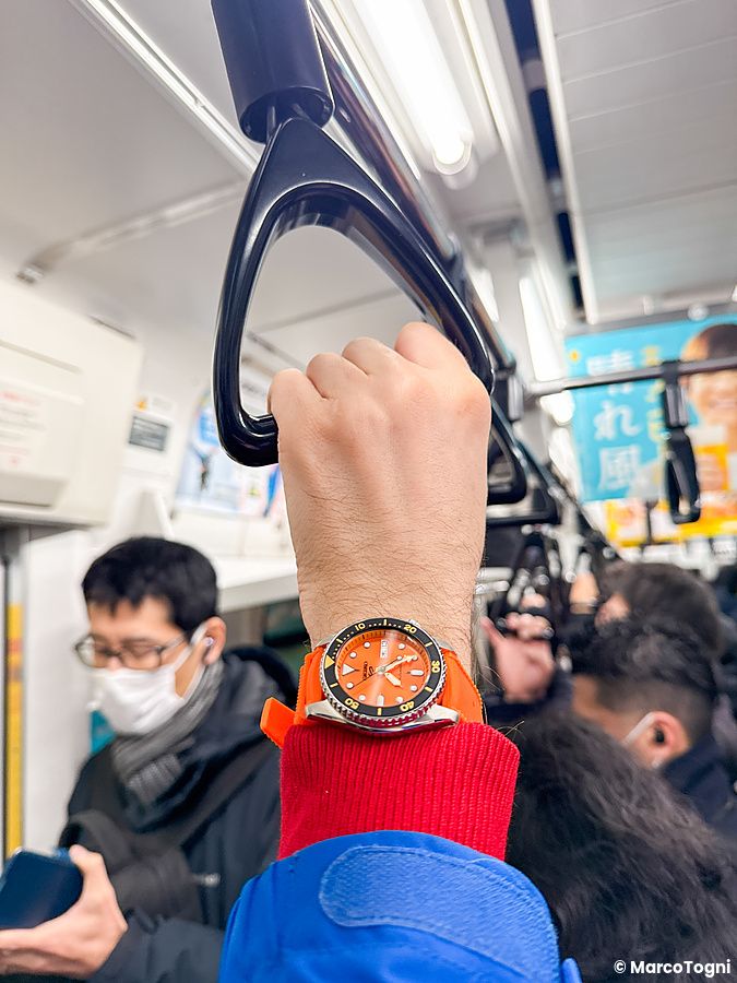 Persona con orologio Seiko arancione in metro affollata in Giappone.