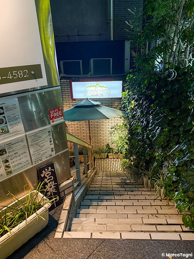 Le scale che portano al ristorante Seven Hills ad Osaka, con insegna luminosa e piante lungo il percorso.