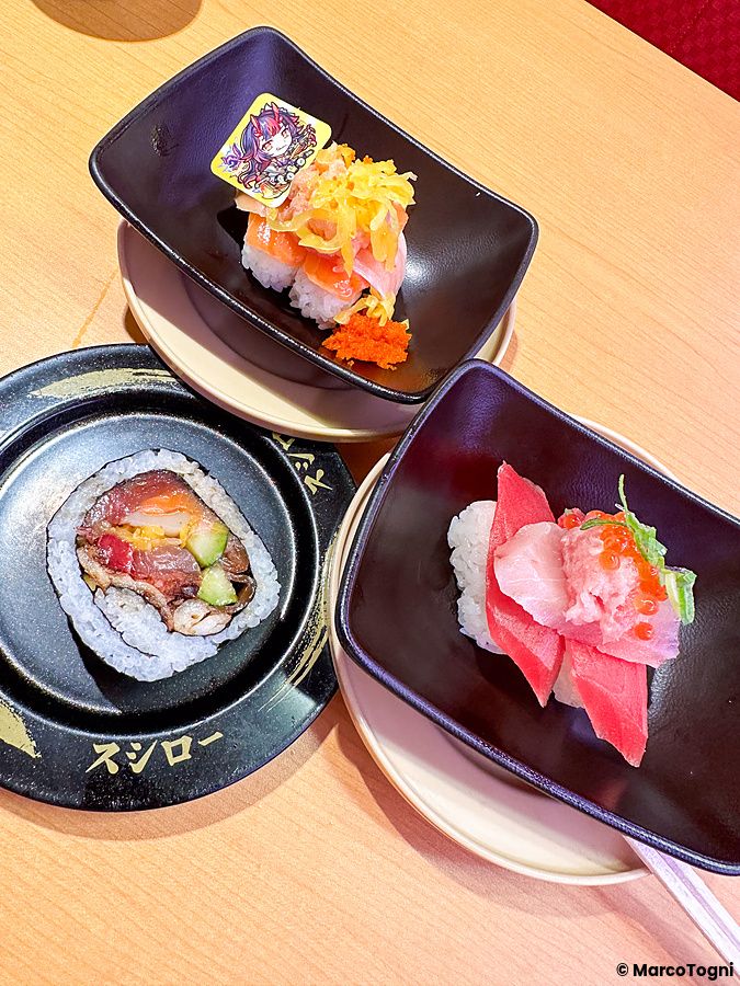 Piatti di sushi serviti su piattini neri con il logo del ristorante Sushiro su un tavolo di legno.