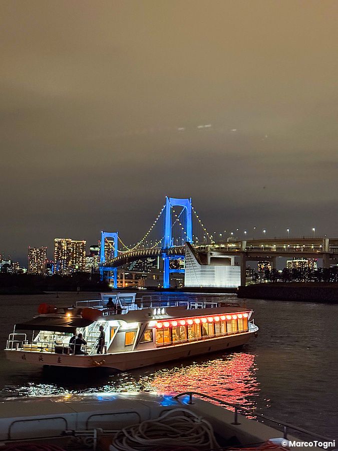 Veduta notturna di una Yakatabune che naviga vicino ad Odaiba, con il Rainbow Bridge illuminato sullo sfondo.