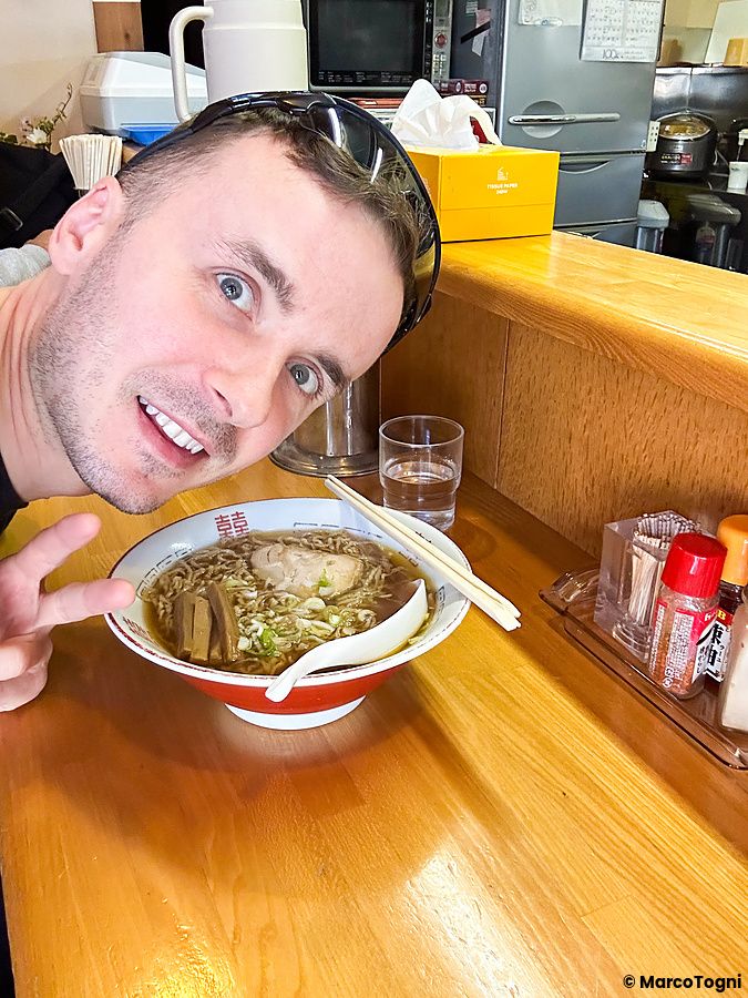 Marco Togni sorridente posa con una ciotola di ramen al bancone del ristorante Midoriya Ramen a Hirosaki.