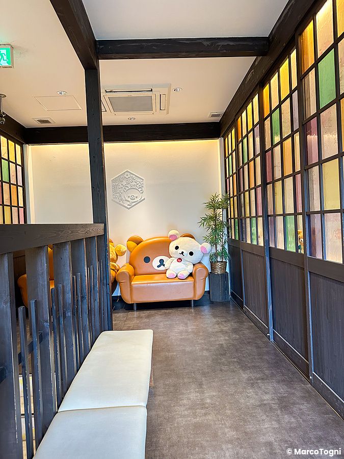 Interno della Rilakkuma Tea house ad Arashiyama con divano e peluche di Rilakkuma tra pannelli in legno e vetri colorati.