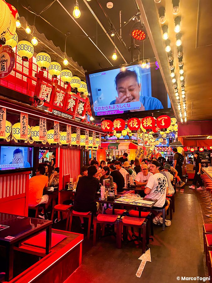 Interno di un ristorante nella Kabukicho Tower a Shinjuku illuminato da lanterne con persone sedute ai tavoli.