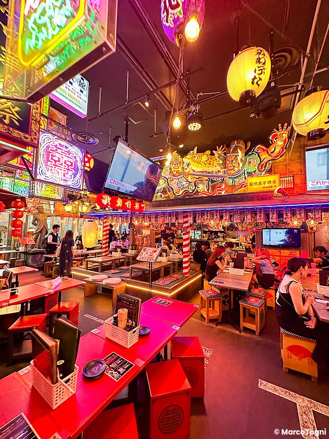 Interno di un ristorante illuminato da neon e lanterne nella Kabukicho Tower a Shinjuku con persone ai tavoli.