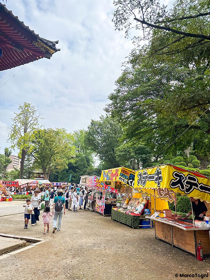 Persone camminano tra bancarelle di cibo di strada all'interno del santuario Nezu a Tokyo, in Giappone.