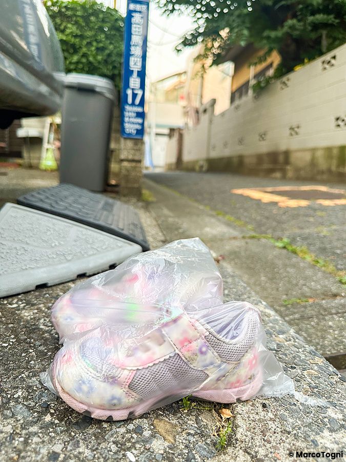 Un paio di scarpe per bambini in un sacchetto di plastica abbandonate su un marciapiede in Giappone.