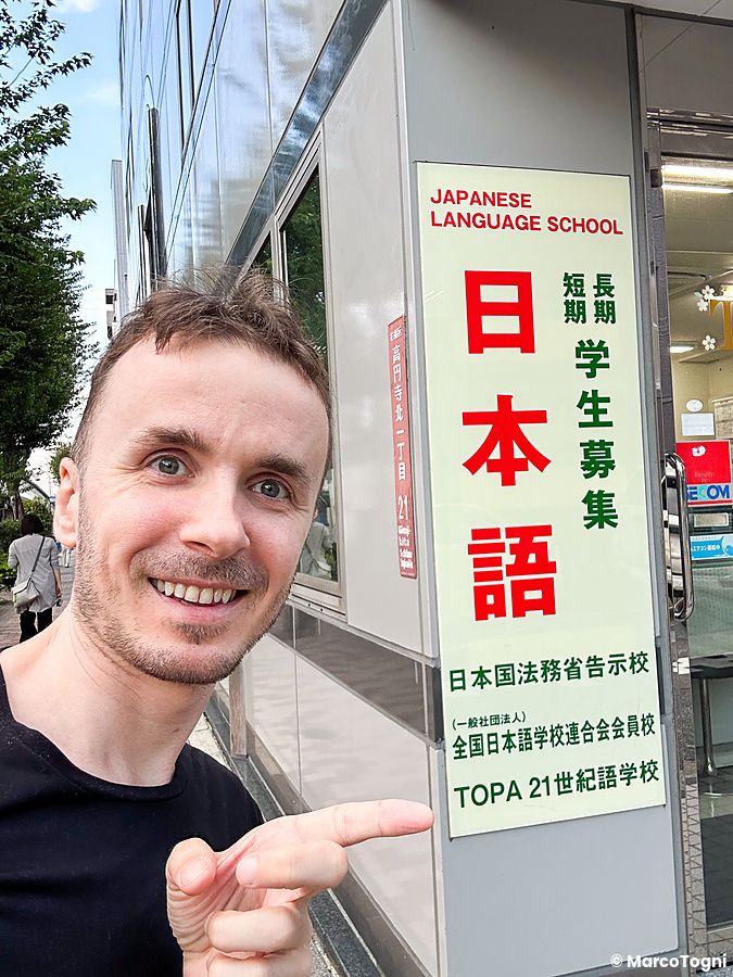 Marco Togni sorridente davanti a una scuola di lingua in Giappone.
