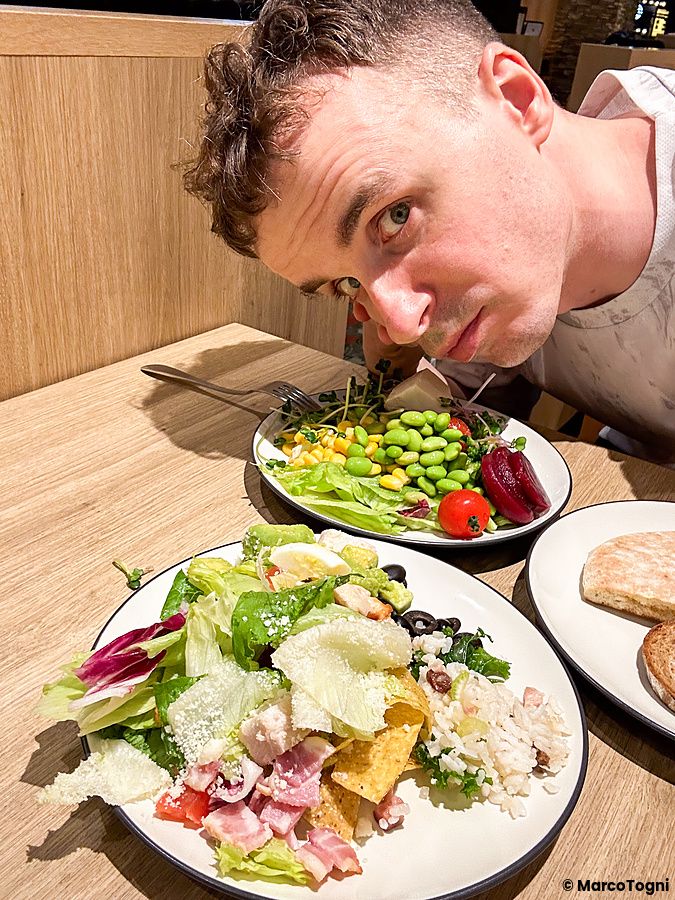 Marco Togni guarda verso l'obiettivo seduto a un tavolo con piatti di insalata presso Sizzler a Tokyo.