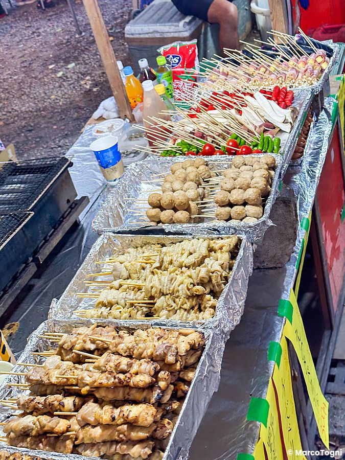 Una bancarella di spiedini street food giappone con vassoi di alluminio pieni di carne e verdure pronte in Giappone.