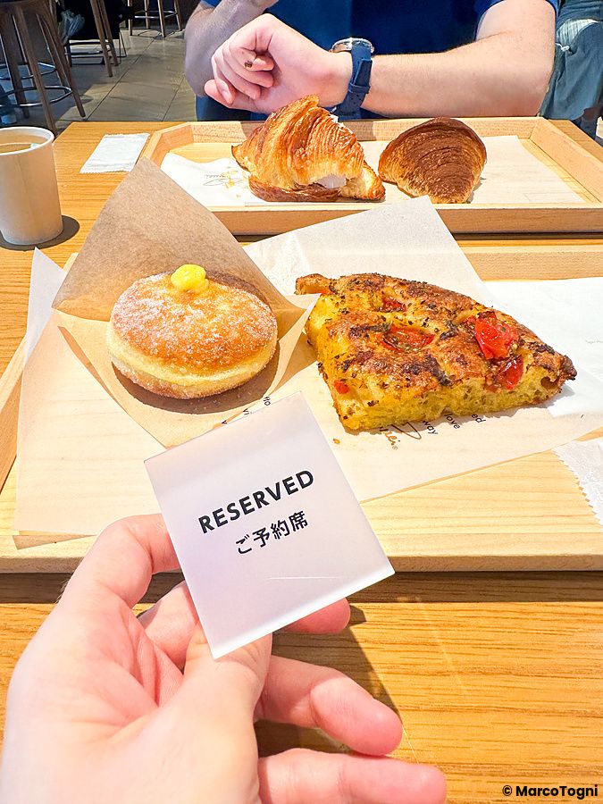 Un cartellino con scritto "RESERVED" tenuto in mano presso lo Starbucks Reserve a Ginza con dolci e focaccia sul tavolo.