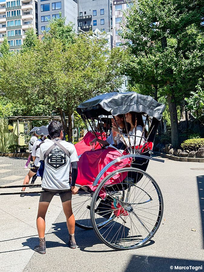 Persona che tira un risciò con due passeggeri in una strada di Asakusa.