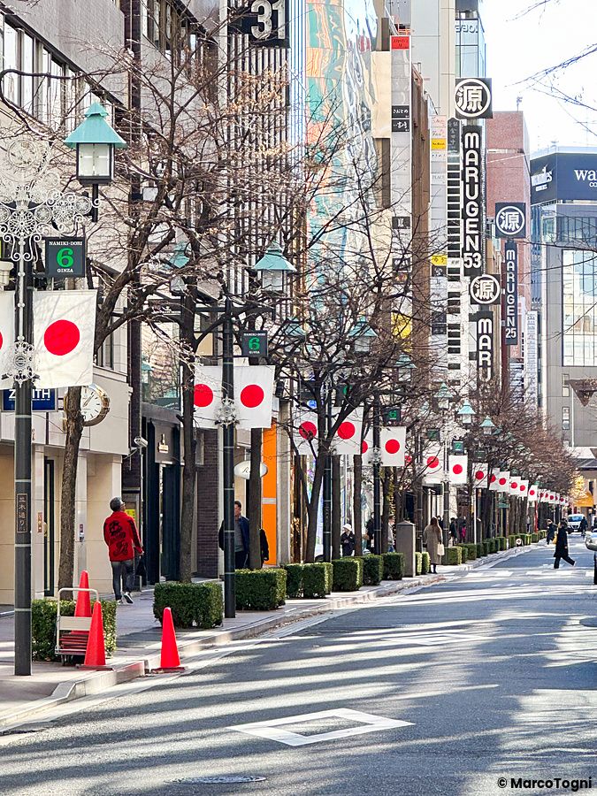 Veduta di una strada alberata nel quartiere di Ginza, a Ginza, decorata con bandiere del Giappone appese ai lampioni.