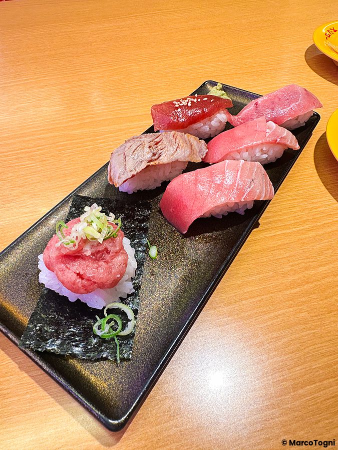 Piatto rettangolare nero con pezzi di tonno misto serviti come sushi a Sushiro su un tavolo di legno chiaro.