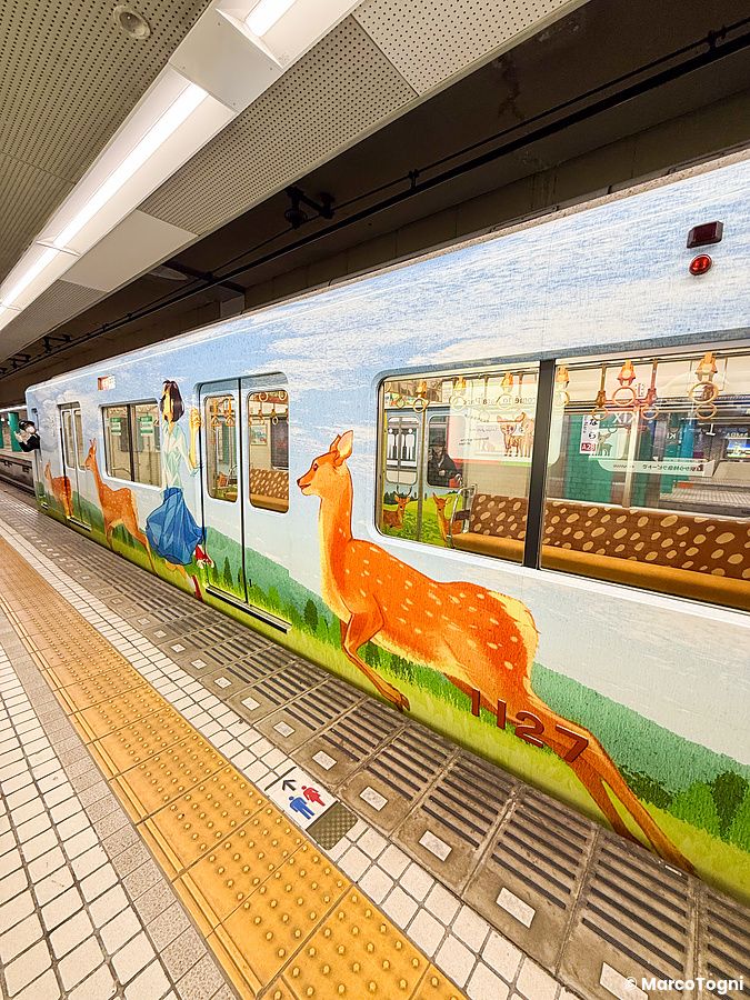 Un treno per Nara decorato con disegni di cervi e una persona lungo la banchina di una stazione.