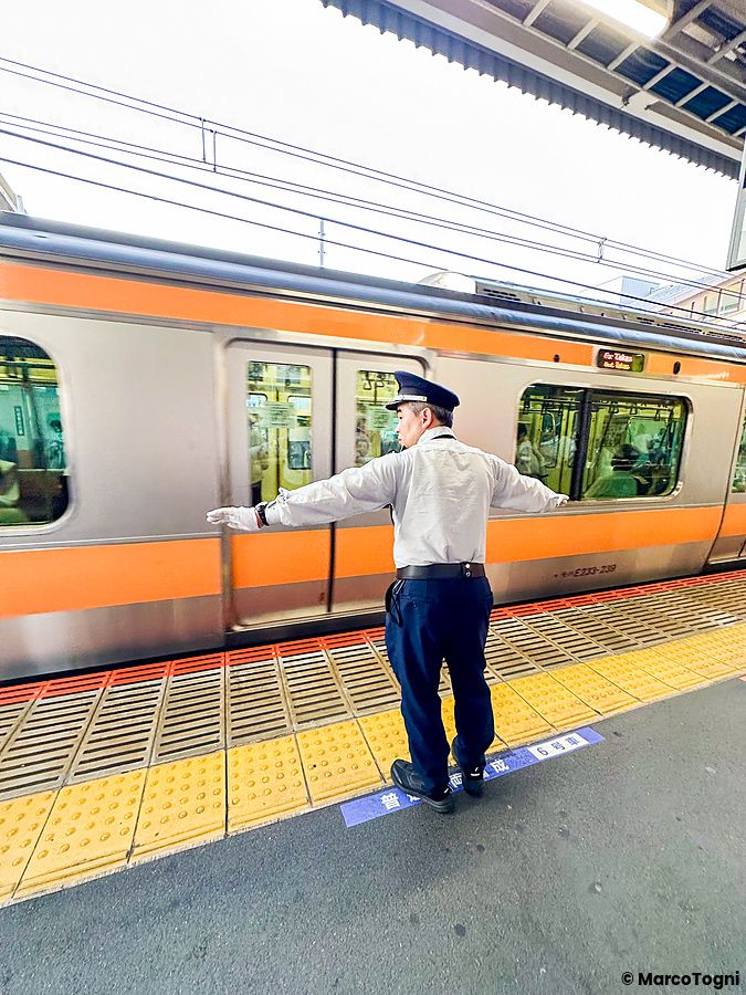 Un uomo in uniforme da capostazione è in piedi sulla banchina di una stazione ferroviaria con le braccia aperte.