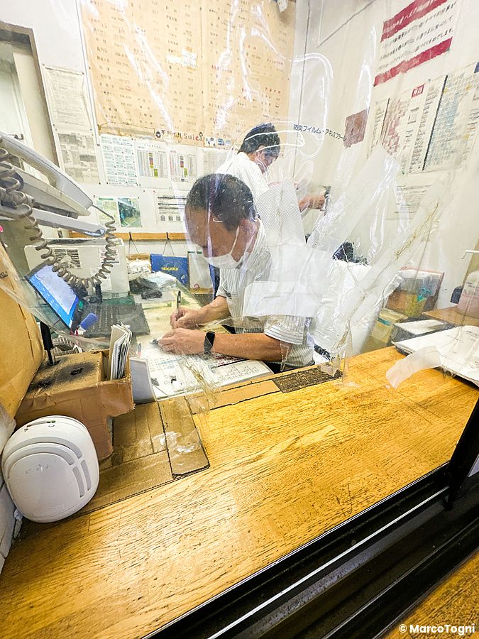 Un impiegato con mascherina lavora dietro un pannello di plastica presso l'ufficio oggetti smarriti in Giappone.