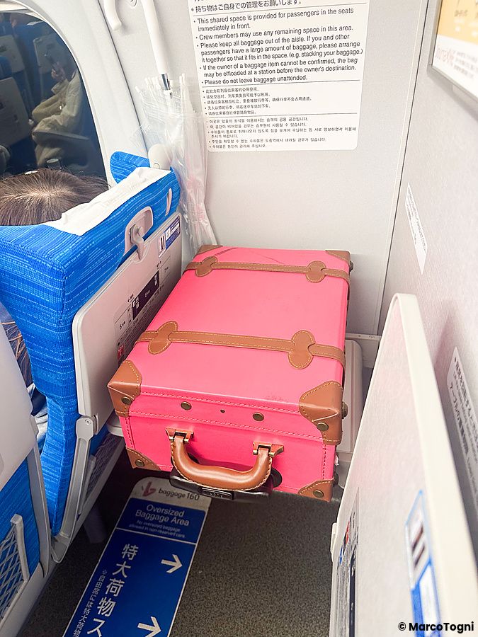 Una valigia rosa vintage posizionata nell'apposito posto per la valigia a sul treno shinkansen.