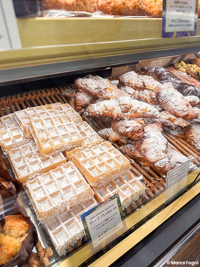 Vetrina di una panetteria Paul in Giappone con waffle al cocco e croissant cosparsi di zucchero a velo.