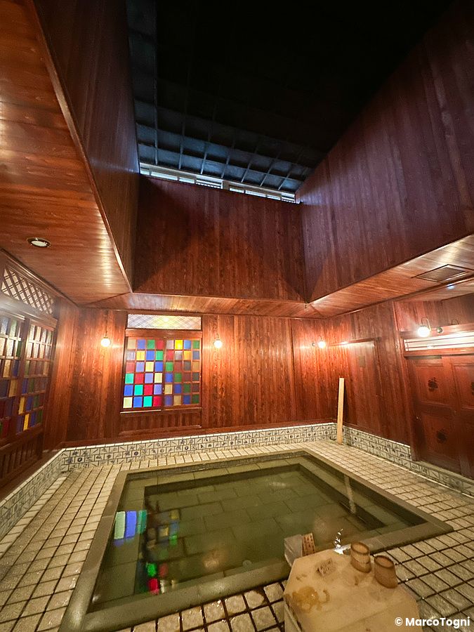 Onsen interno a Yamashiro Onsen con vasca termale e pareti di legno scuro.