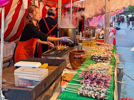 Una donna cuoce spiedini di frutti di mare su una griglia in una bancarella ad Asakusa.