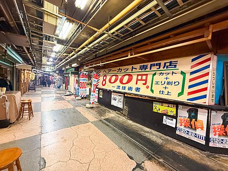 Corridoio sotterraneo dell'Asakusa Underground Street con insegne di un barbiere e manifesti pubblicitari alle pareti.