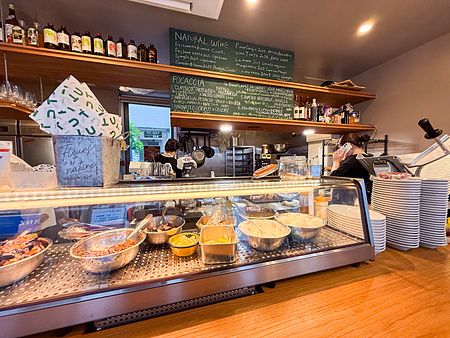 Il bancone a Tutu di Tokyo mostra una vetrina refrigerata con ciotole di ingredienti e menu scritto su lavagna.
