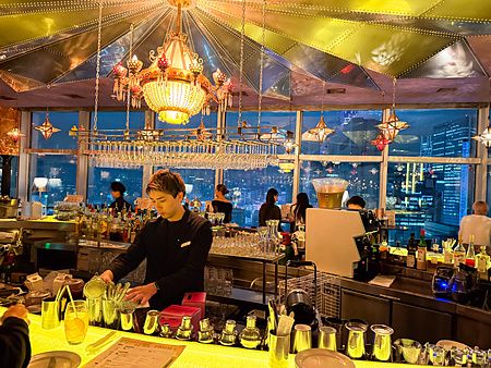 L'interno del Cafe Legato a Shibuya con un barista al bancone e una vista panoramica illuminata sulla città di notte.