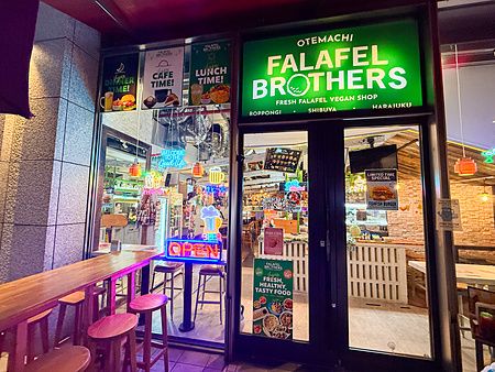 Facciata del ristorante vegano Falafel Brothers a Otemachi, Tokyo, con insegna verde luminosa e bancone esterno.